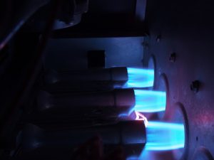 Three natural gas burners with bright blue flames inside an operating gas furnace.
