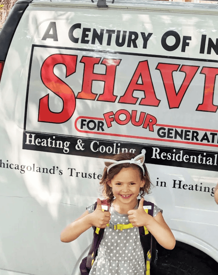 Young girl with bunny ears smiling in front of a Shavitz Heating and Air Conditioning service vehicle.
