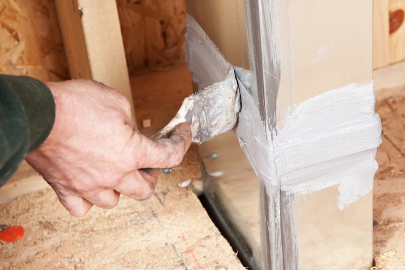 Why Are Some Rooms in My House Always Too Hot or Too Cold? A hand holding a paintbrush, is spreading caulk over a house air duct joint with a paintbrush.
