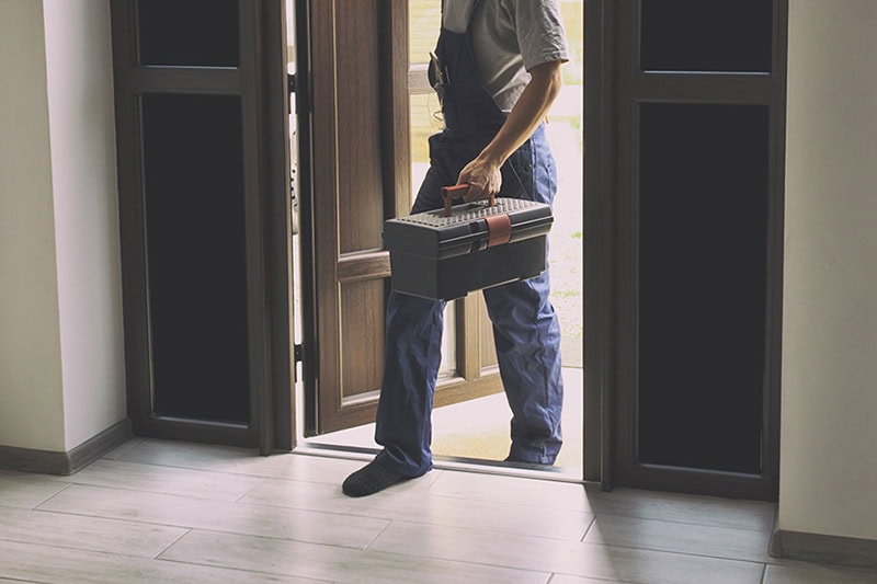 What’s Included in a Professional HVAC Tune-Up? Photo of a maintenance technician walking into a home carrying tools.